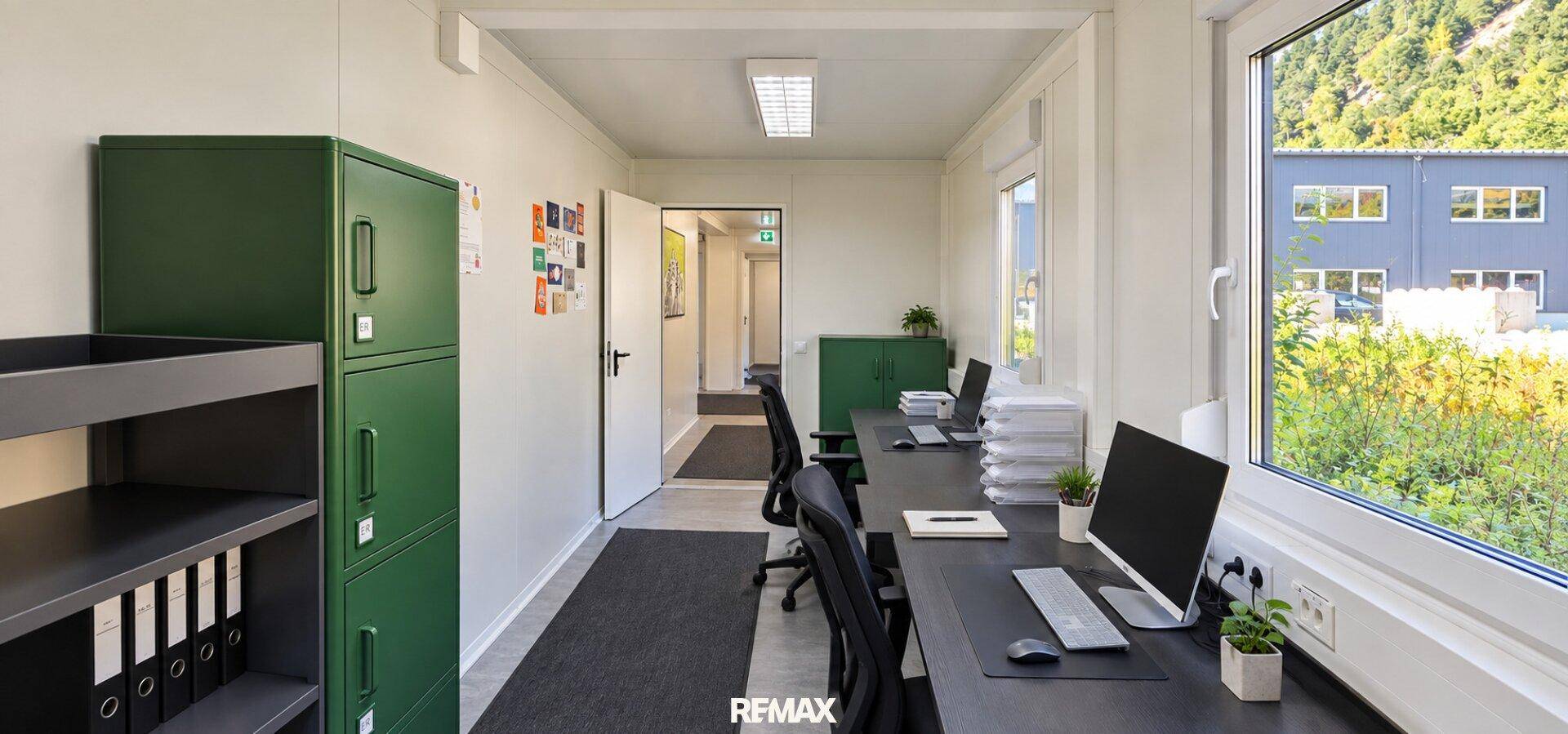Helles Büro in einem Containergebäude mit mehreren Arbeitsplätzen, grünen Schränken und Fenstern.