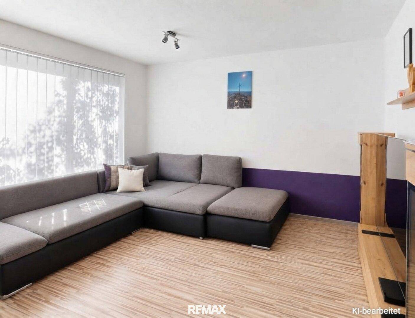 Gemütliches Wohnzimmer mit großem Ecksofa, Laminatboden und farbiger Akzentwand.