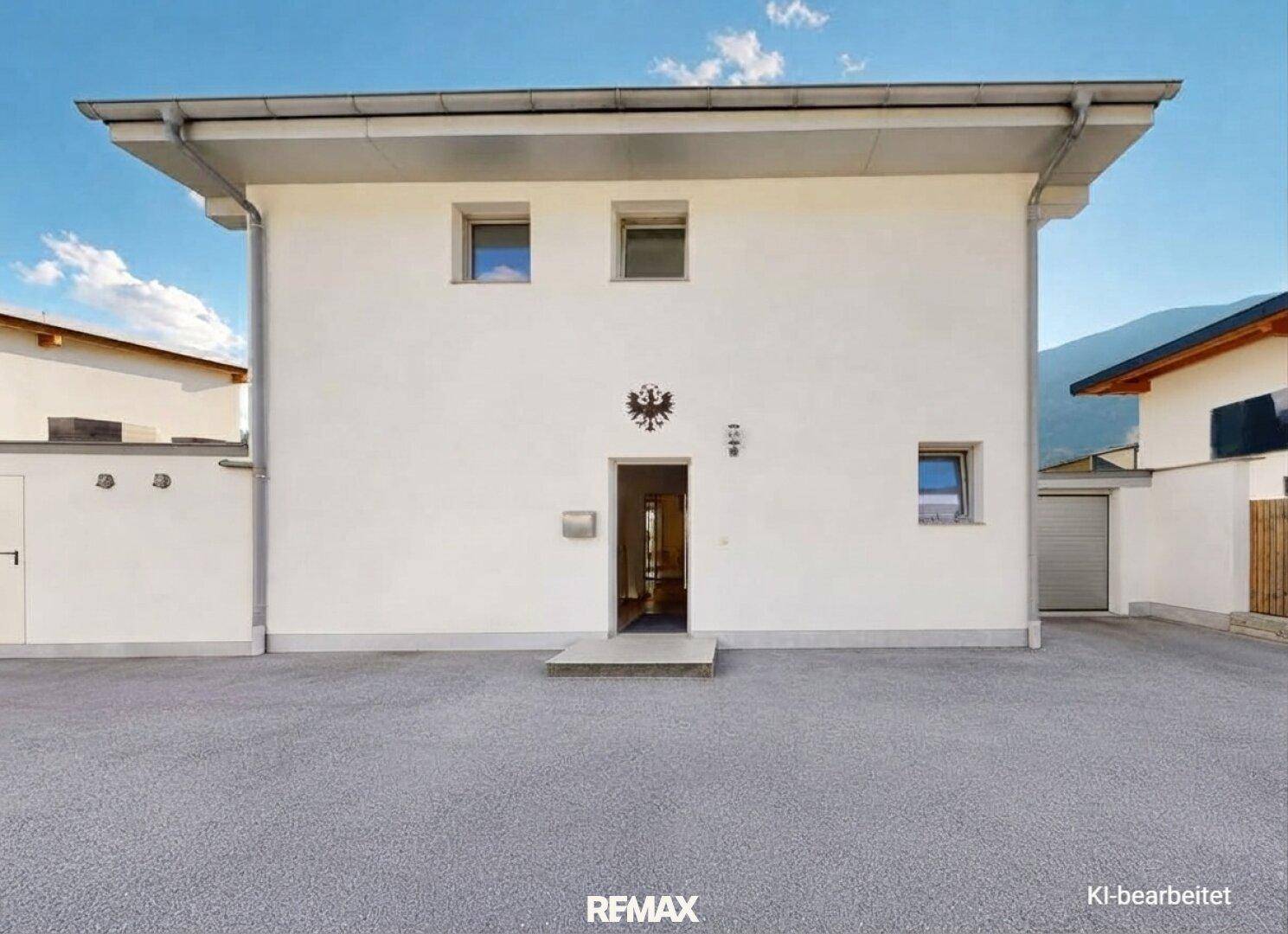 Vorderansicht eines Einfamilienhauses mit weißer Fassade und großem gepflasterten Vorplatz.