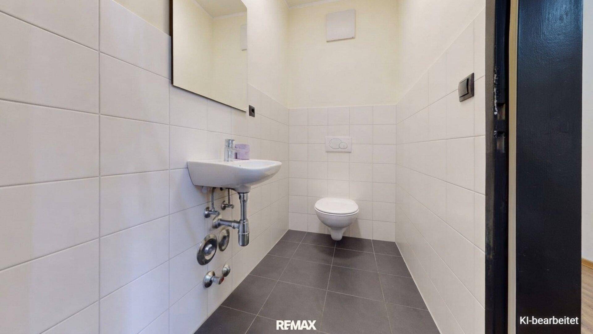 Funktionale Gästetoilette mit wandhängendem WC, kleinem Waschbecken und Fliesenboden.