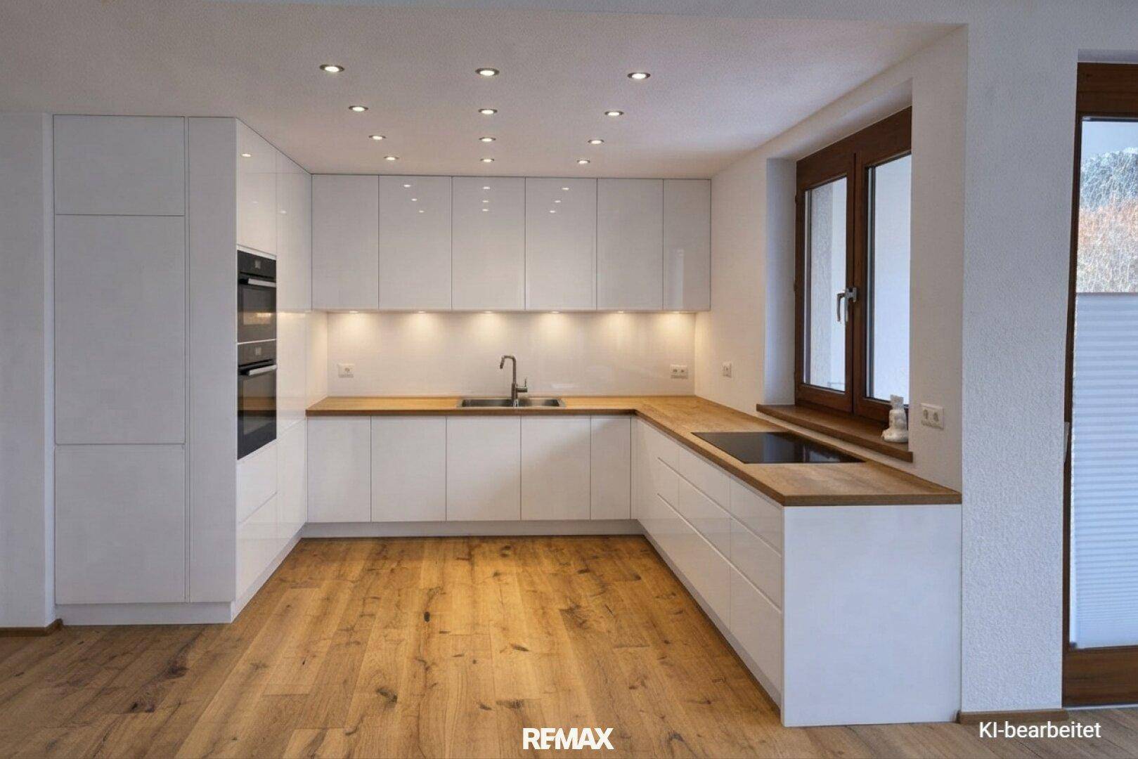 Moderne weiße Küche mit Holz-Arbeitsplatten, Einbaugeräten und integrierter Beleuchtung.