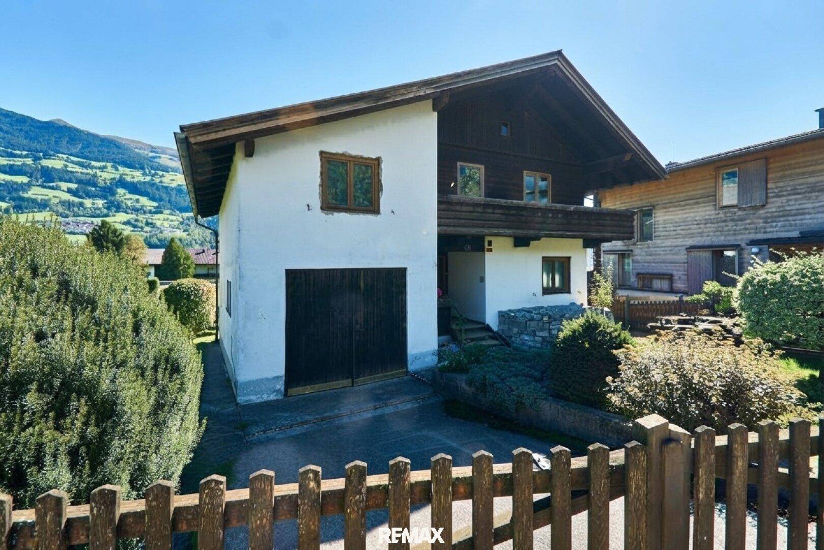 Hausfassade mit integrierter Garage, umgeben von einem grünen Garten und mit Blick auf die Berge.