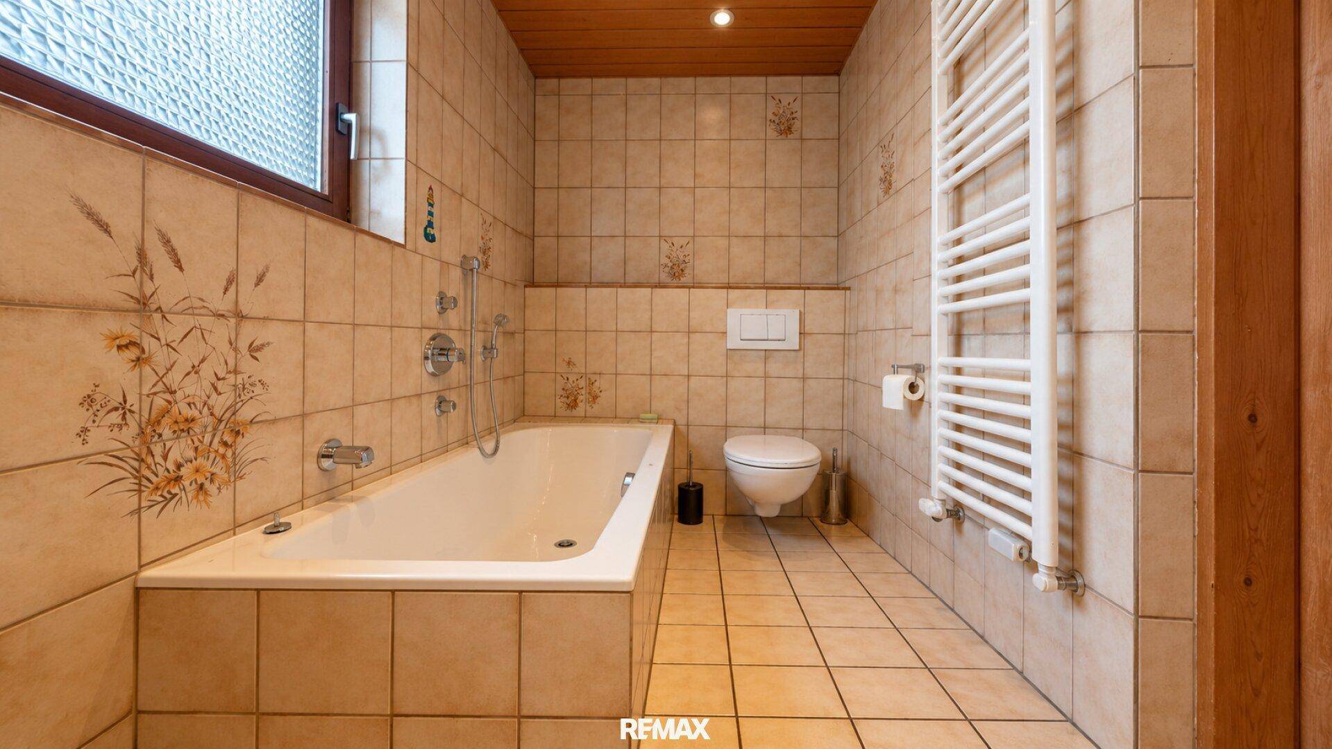 Traditionelles Badezimmer mit Badewanne, WC und beheiztem Handtuchhalter, gefliest in Beige.