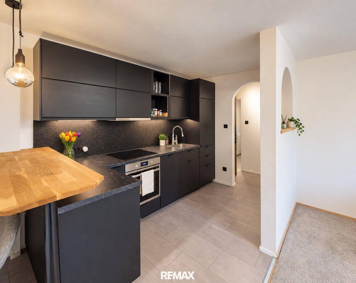Moderne schwarze Küche mit Holztheke, Induktionskochfeld und integriertem Backofen.