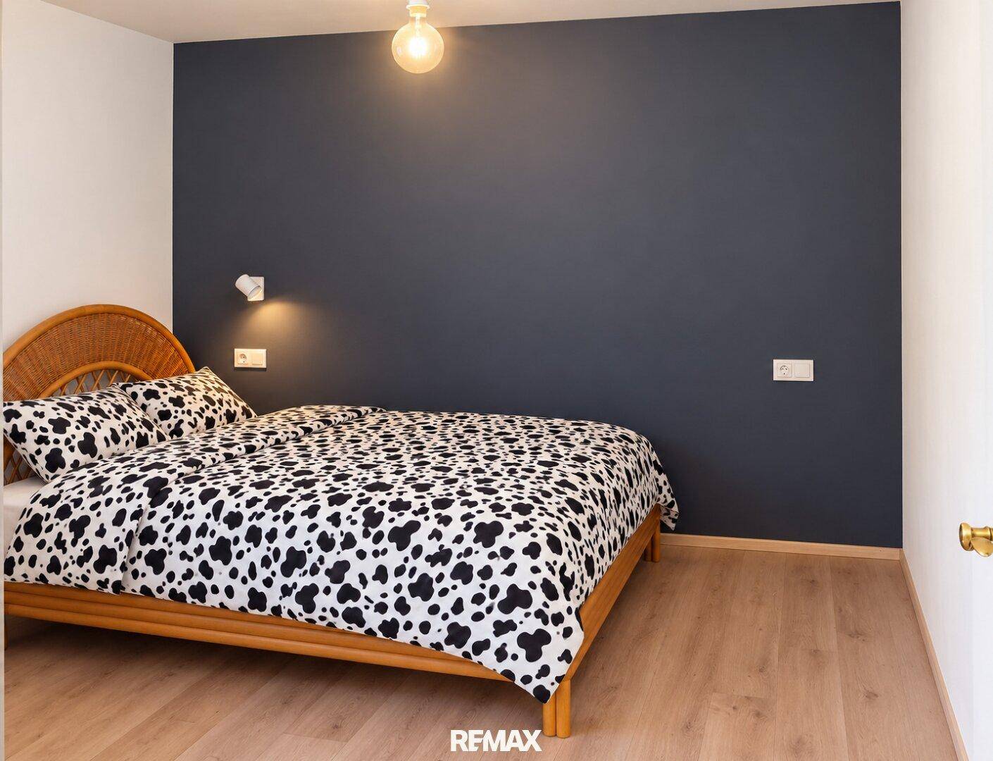 Schlafzimmer mit dunkler Akzentwand, Holzbett und gemustertem Bettzeug.