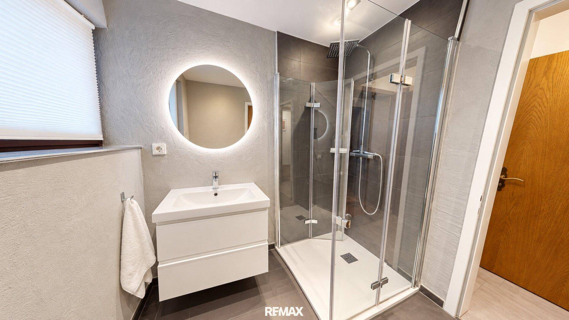 Modernes Badezimmer mit begehbarer Dusche, beleuchtetem Spiegel und schwebendem Waschtisch.