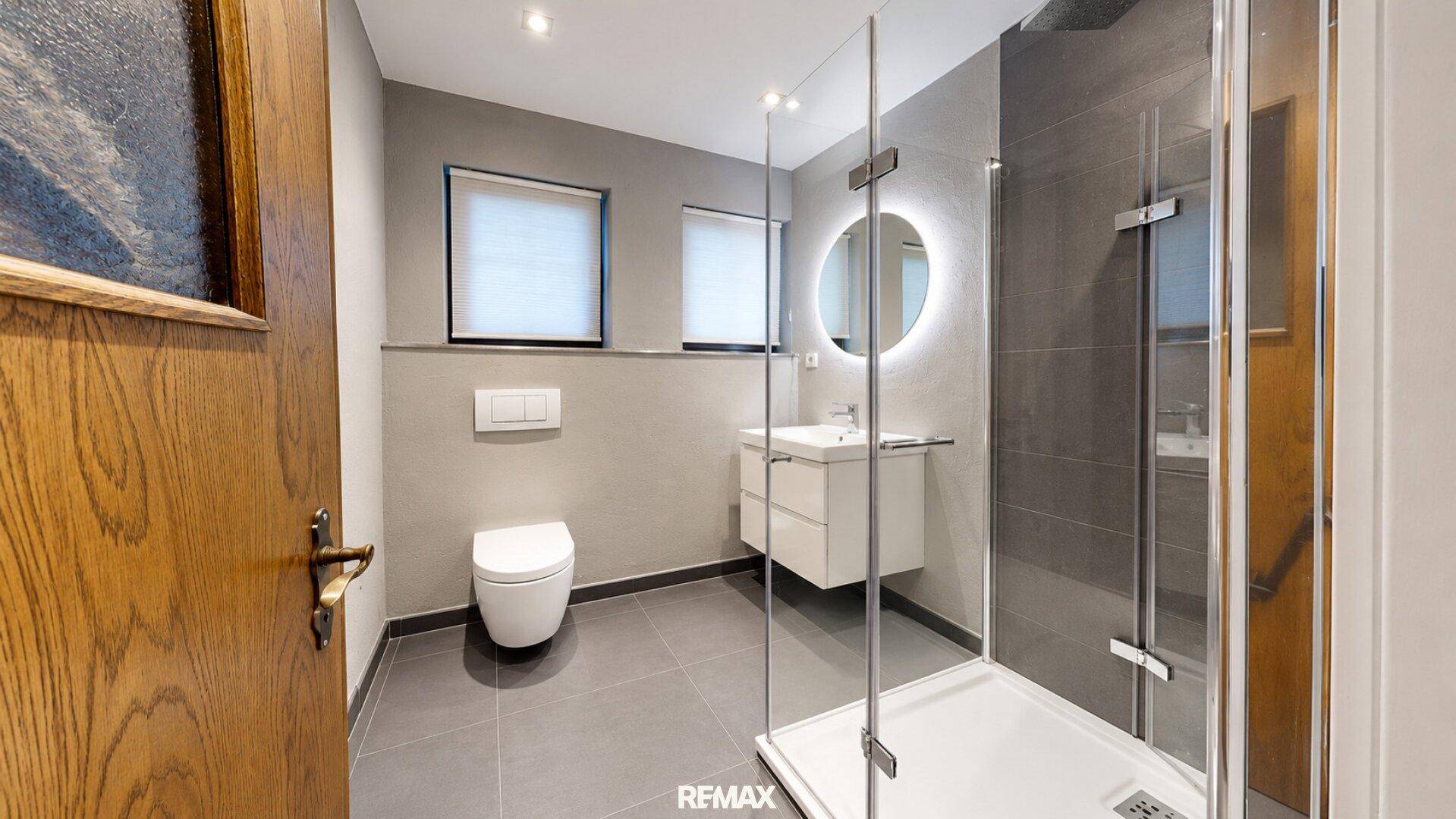 Elegantes Badezimmer mit begehbarer Dusche, Wand-WC und beleuchtetem Spiegel.