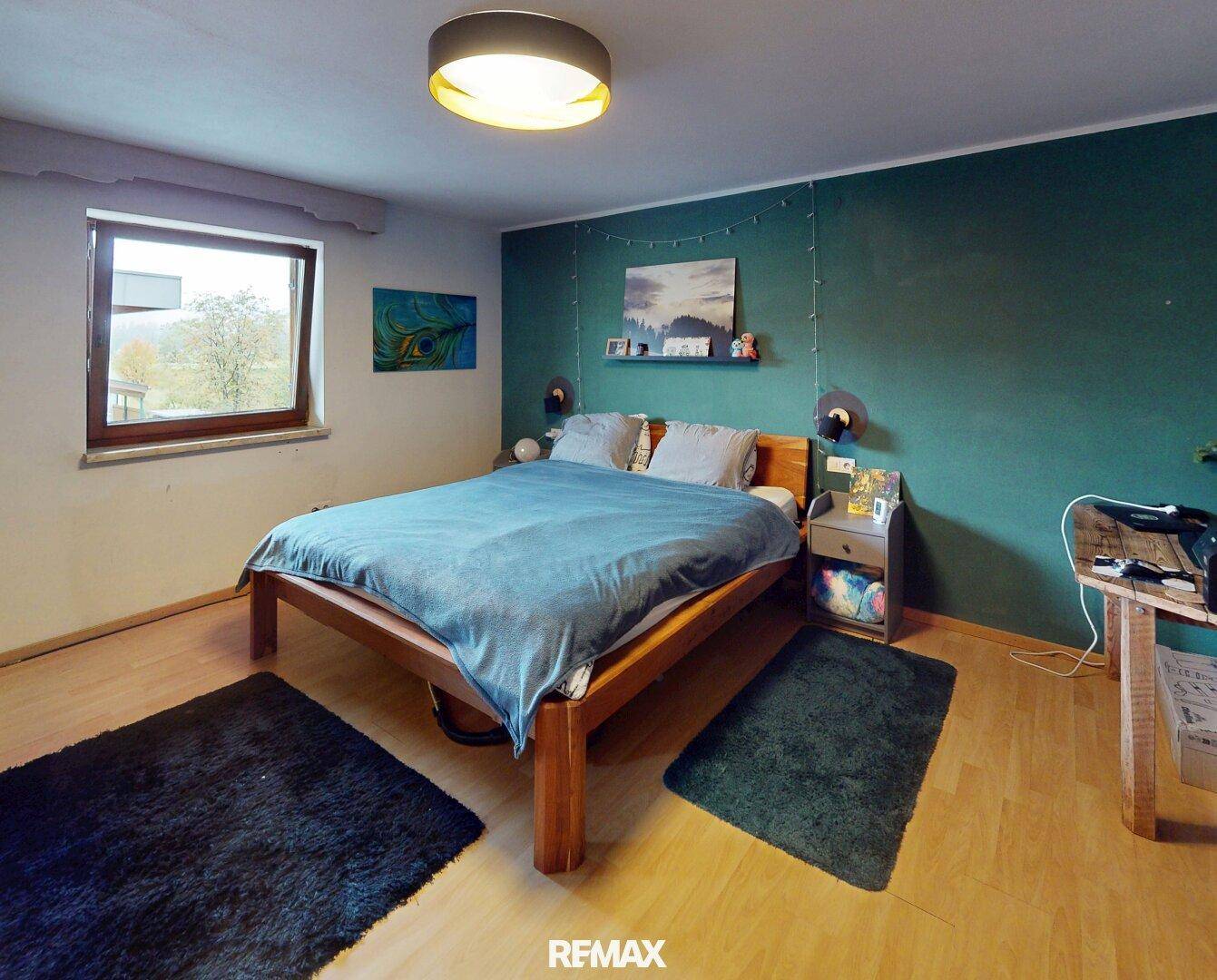 Modern eingerichtetes Schlafzimmer mit Holzbett, grüner Akzentwand und Blick ins Grüne.