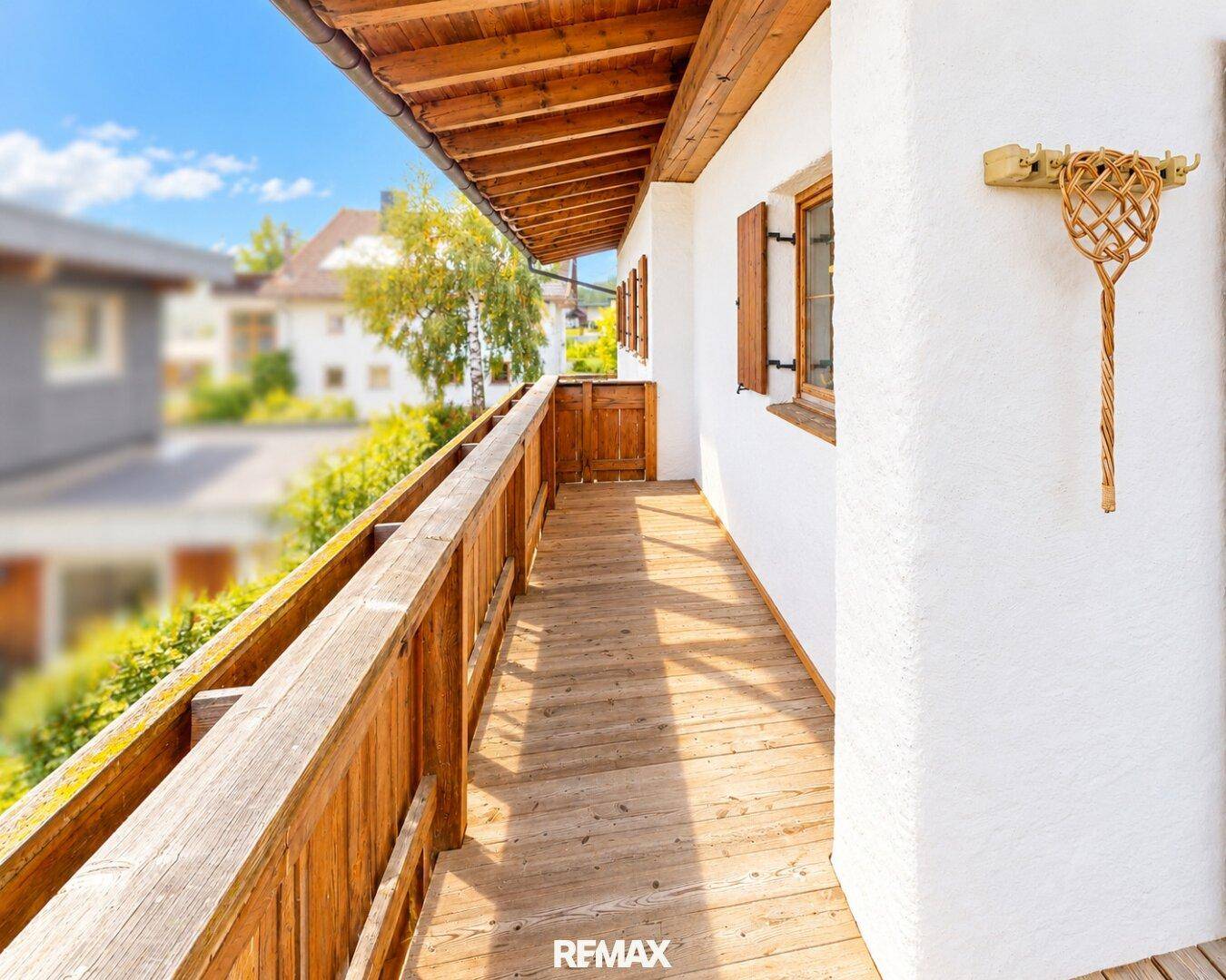 Sonniger Balkon mit Holzgeländer und Holzboden, umgeben von grüner Natur.
