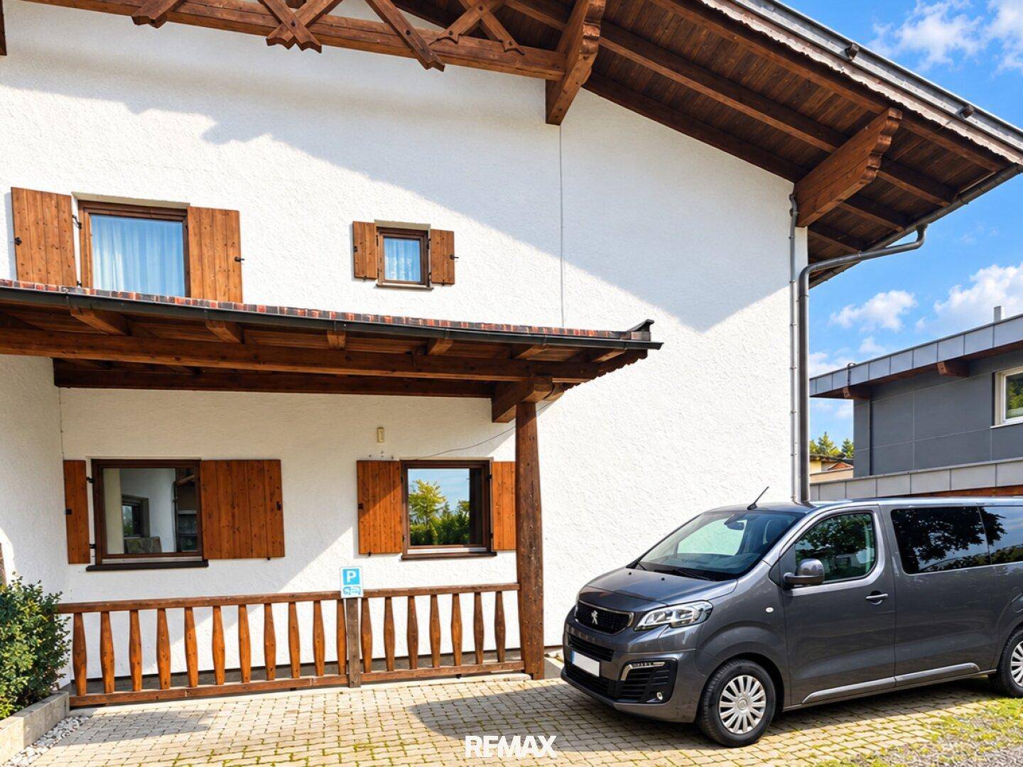 Traditionelles Haus mit weißer Fassade, Holzfensterläden und gepflastertem Parkplatz davor.