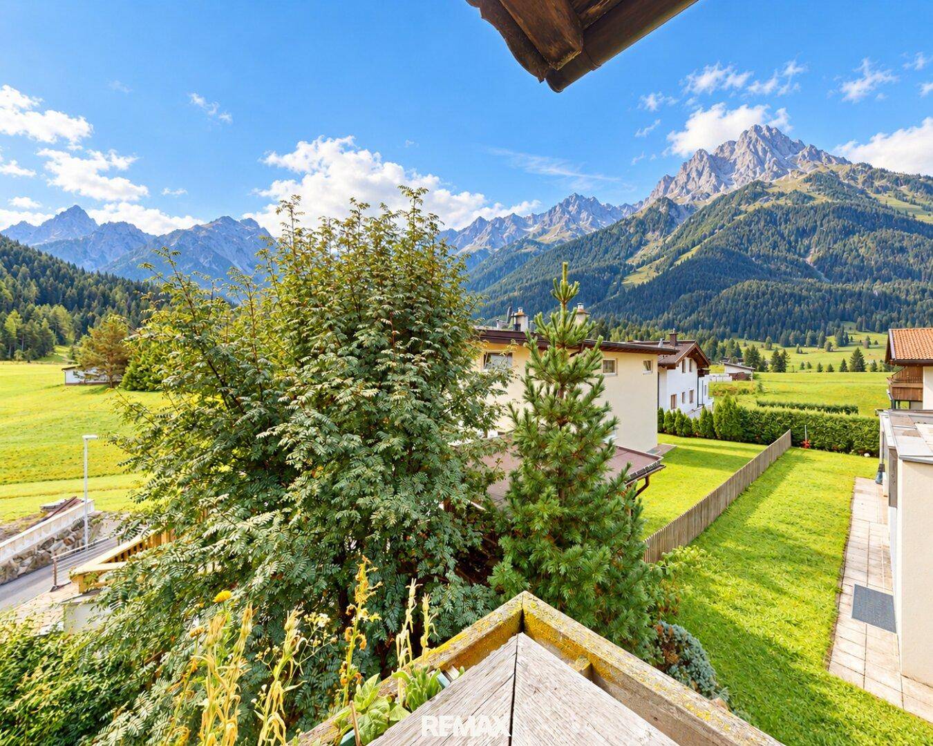 Atemberaubender Bergblick über grüne Wiesen und Bäume von einem sonnigen Balkon.