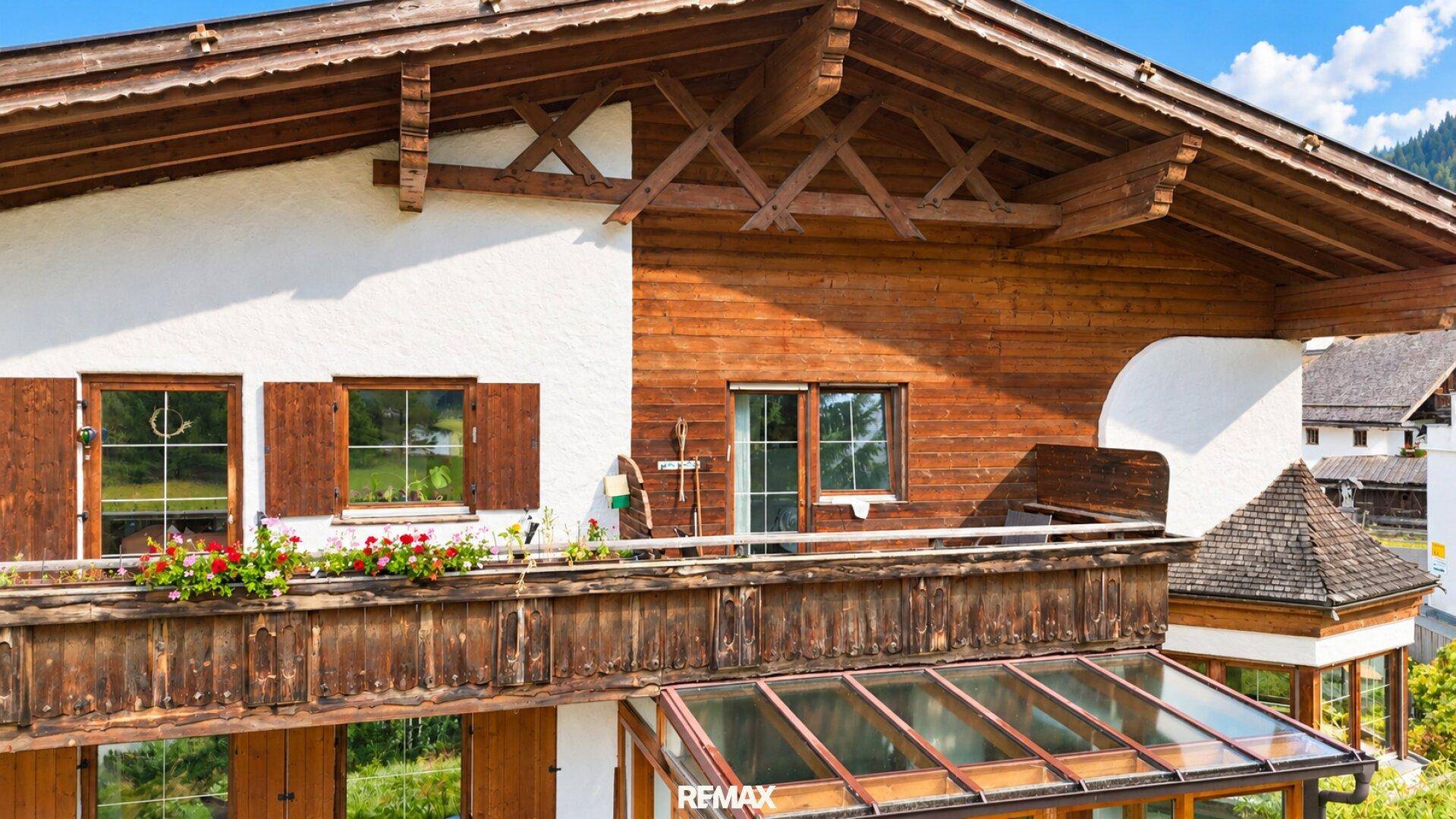 Detailansicht der Hausfassade mit Holzbalkon, Blumenkästen und einem Wintergarten darunter.