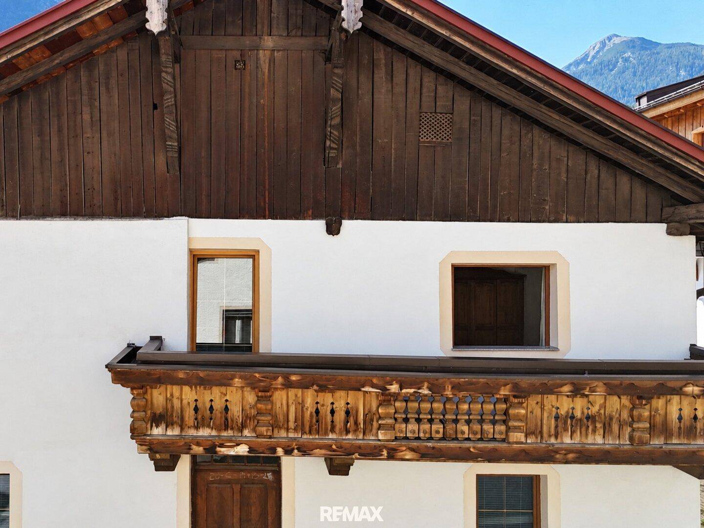 Detailansicht eines traditionellen Holzbalkons mit kunstvollen Schnitzereien an einer weiß verputzten Fassade.