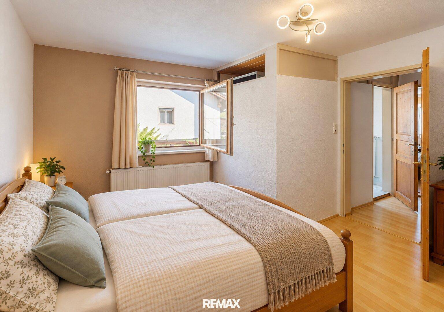 Helles Schlafzimmer mit Doppelbett, Holzboden und einem Fenster, das viel Tageslicht hereinlässt.