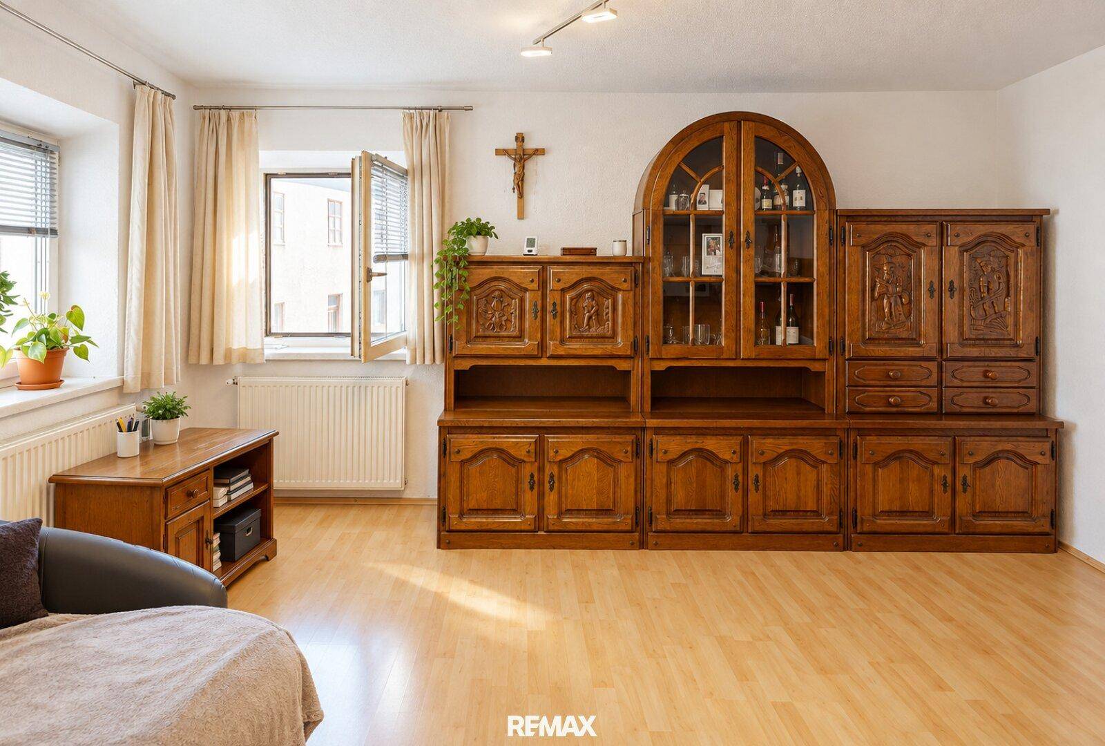 Geräumiges Wohnzimmer mit traditionellen Holzmöbeln, Holzboden und einem Fenster mit Blick nach draußen.