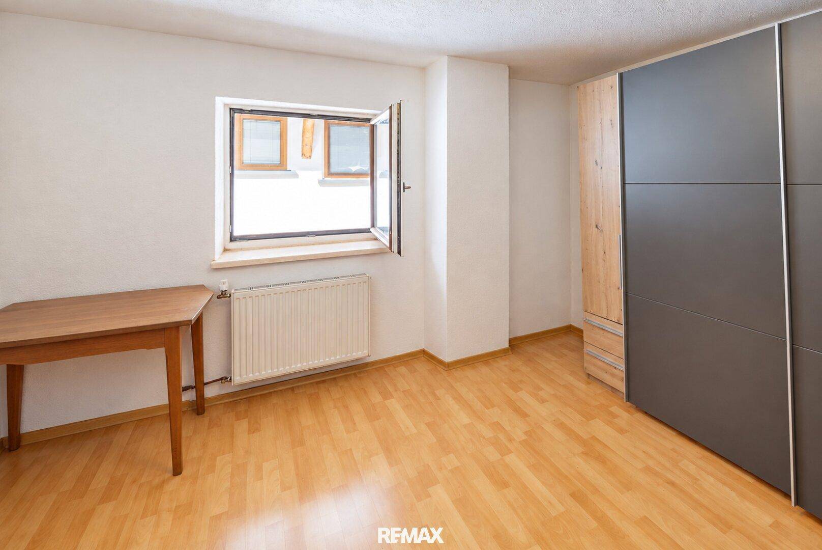 Helles Zimmer mit Holzboden, einem großen Fenster und einem modernen Kleiderschrank mit Holzdetails.