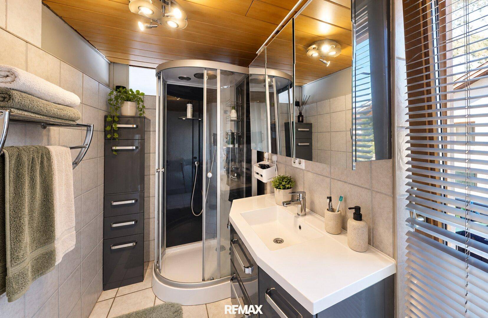 Modernes Badezimmer mit Duschkabine, Waschtisch und Holzdecke, gut beleuchtet und funktional.