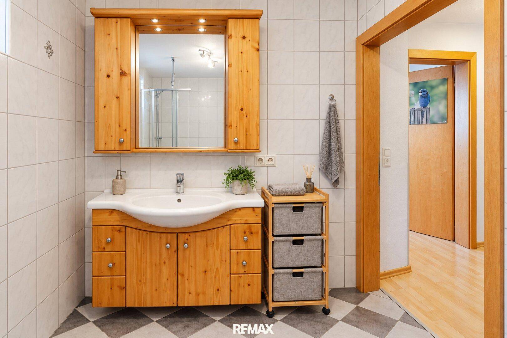 Badezimmer mit Holzwaschtischunterschrank, Spiegelschrank und hellen Fliesen.