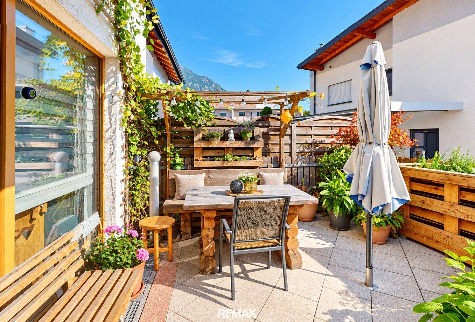 Sonniger Terrassenbereich mit rustikalen Holzmöbeln und üppiger Bepflanzung.