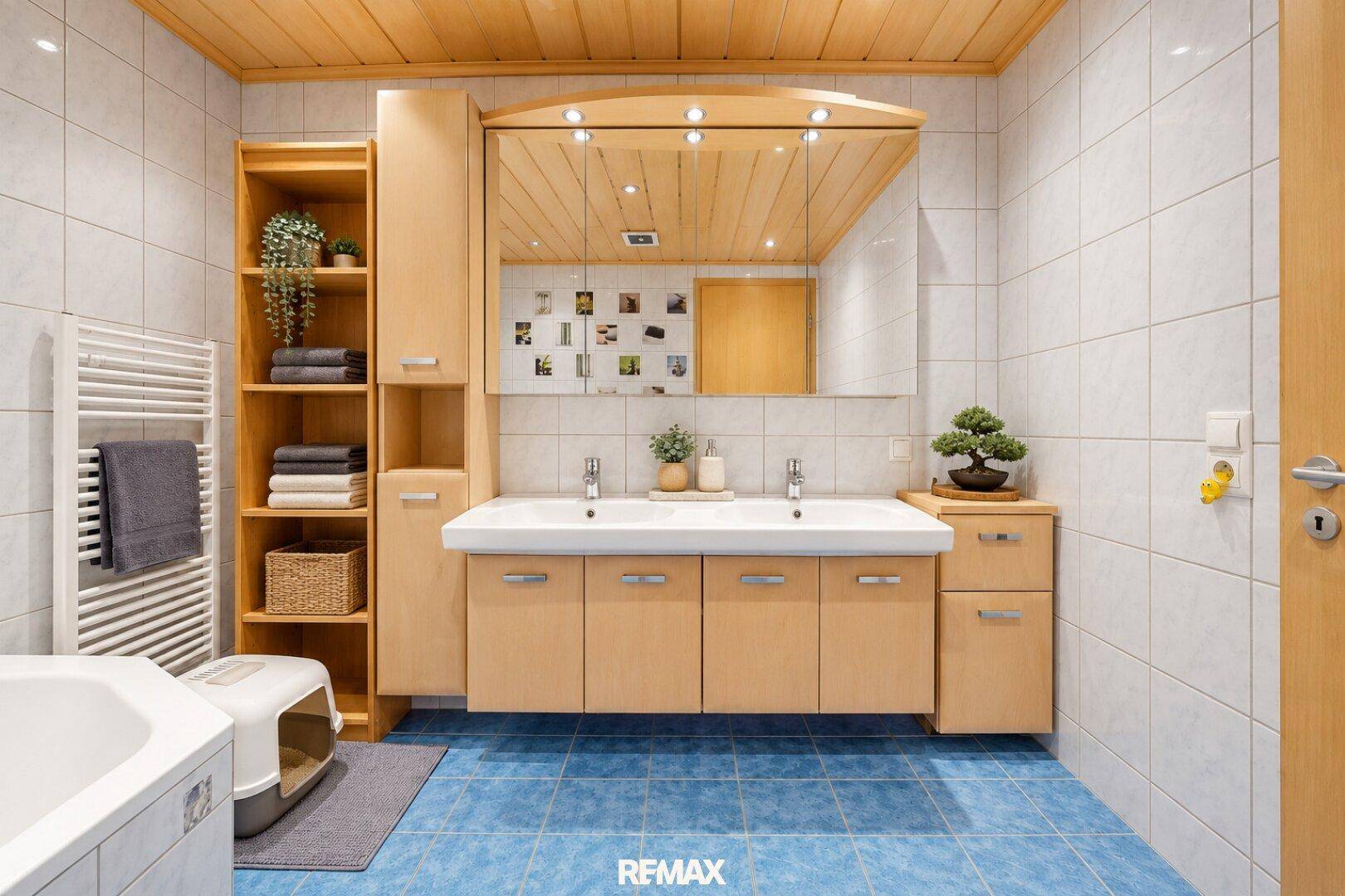 Geräumiges Badezimmer mit Doppelwaschbecken, Badewanne und blauen Bodenfliesen.