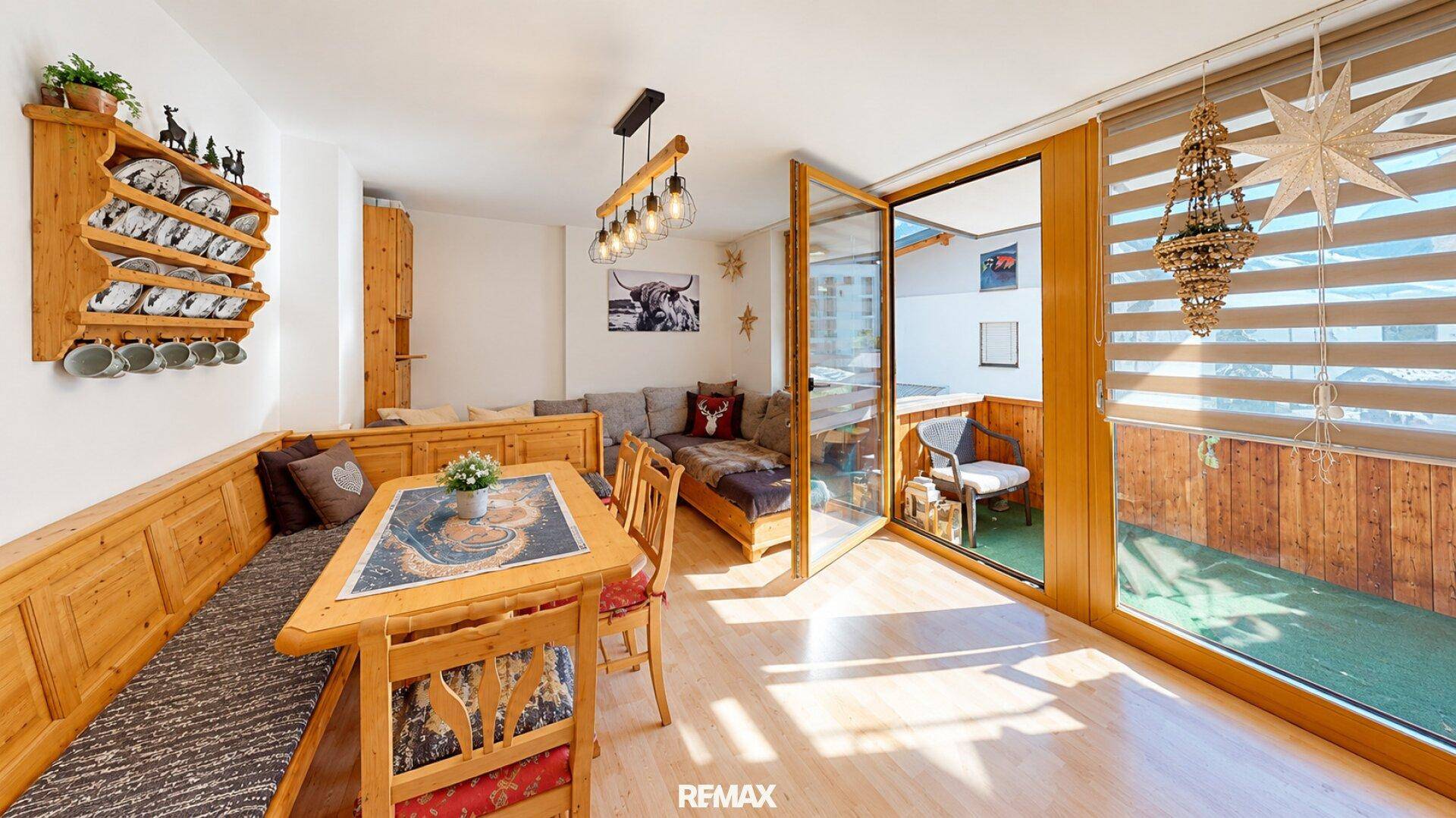 Gemütlicher Wohn-Essbereich im alpinen Stil mit Holzbänken und Zugang zum Balkon.