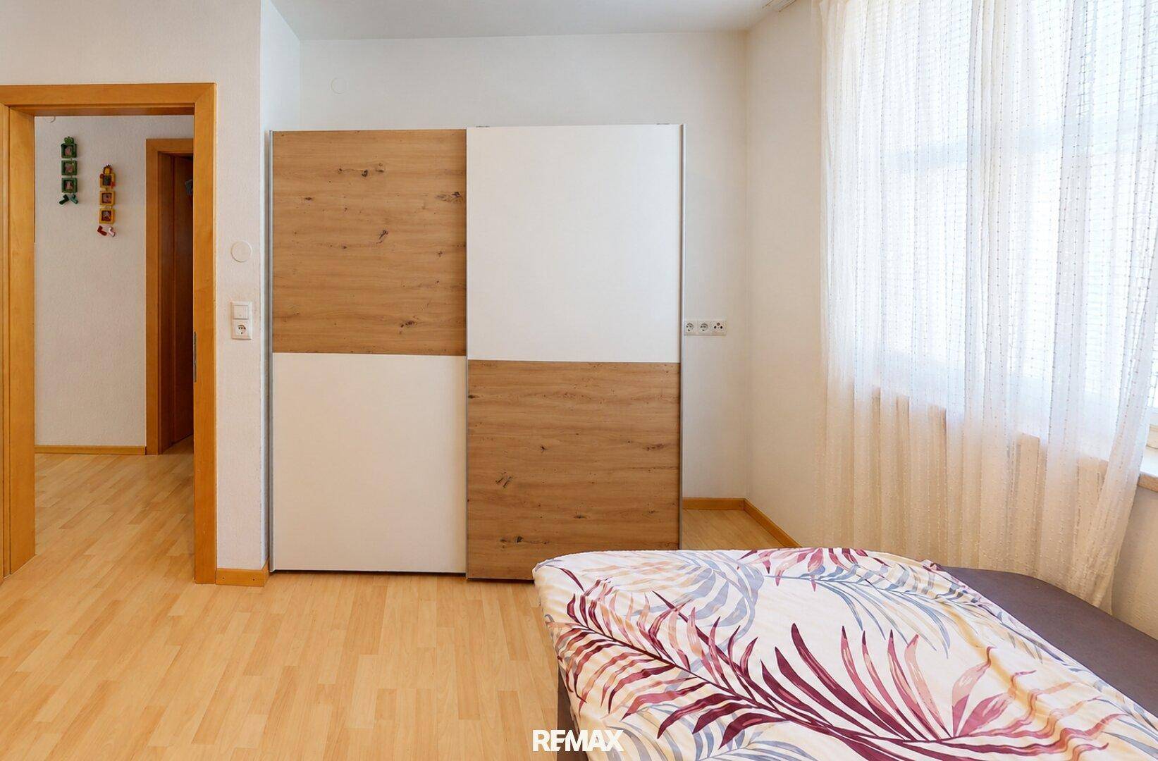 Schlafzimmer mit Schiebetürenschrank und hellem Holzfußboden.