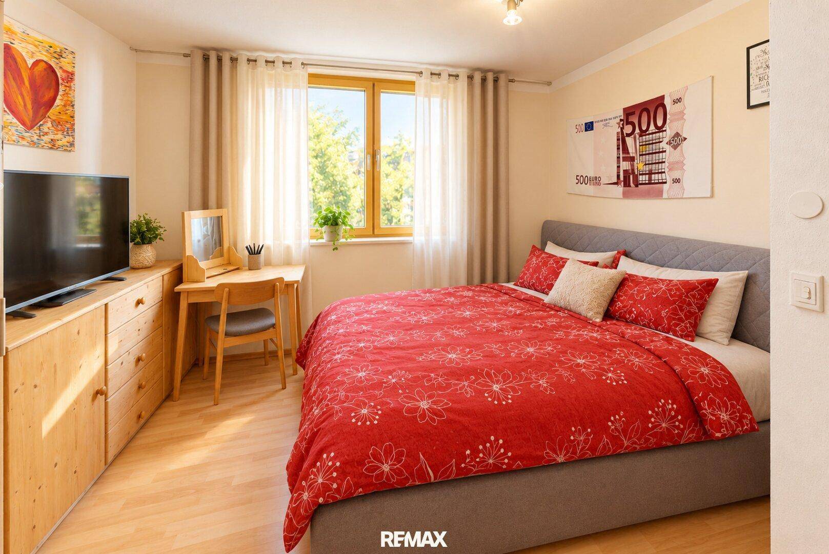 Schlafzimmer mit Doppelbett, Kommode und Schreibtisch am Fenster.