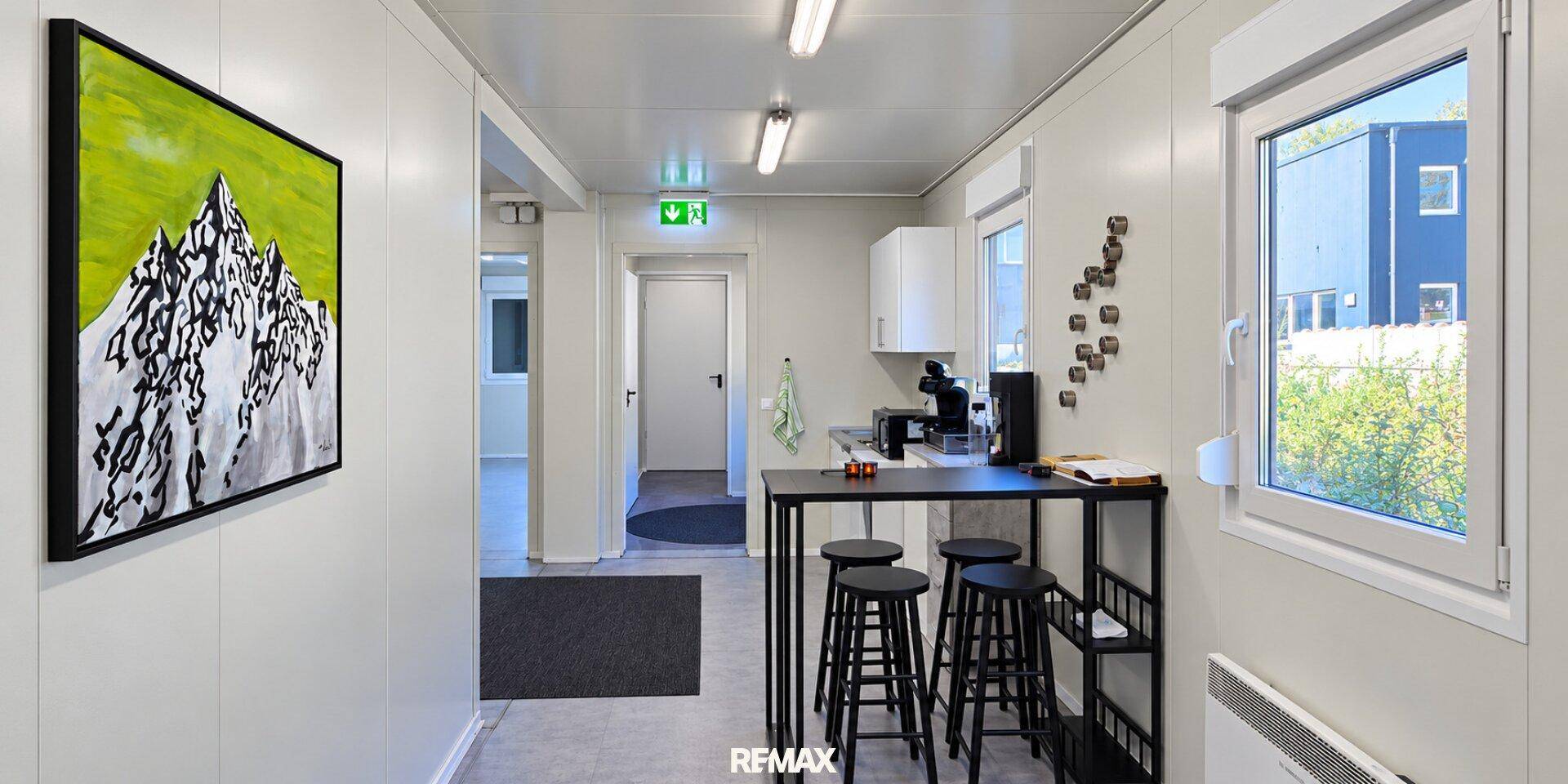 Moderner Büro- oder Aufenthaltsbereich in einem Containergebäude mit kleiner Küchenzeile und Kunstwerk.