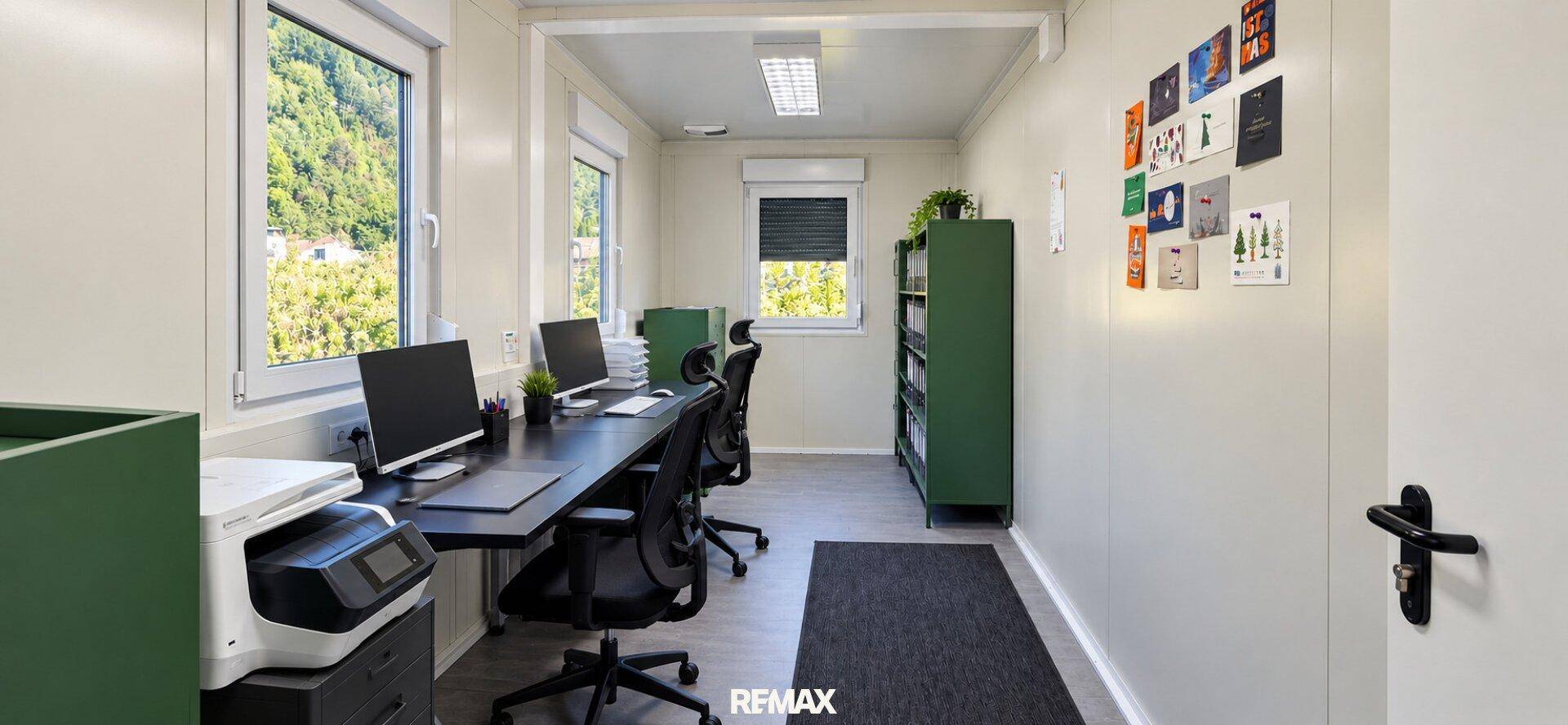 Funktionales Büro in einem Container mit Schreibtischen, Computern und grünen Regalen, hell und modern.