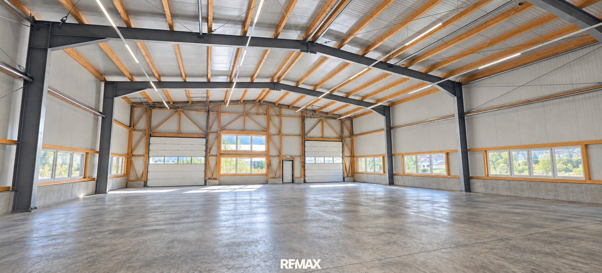 Weitläufige Lagerhalle mit hohen Decken, Rolltoren und großen Fenstern, die viel Licht hereinlassen.