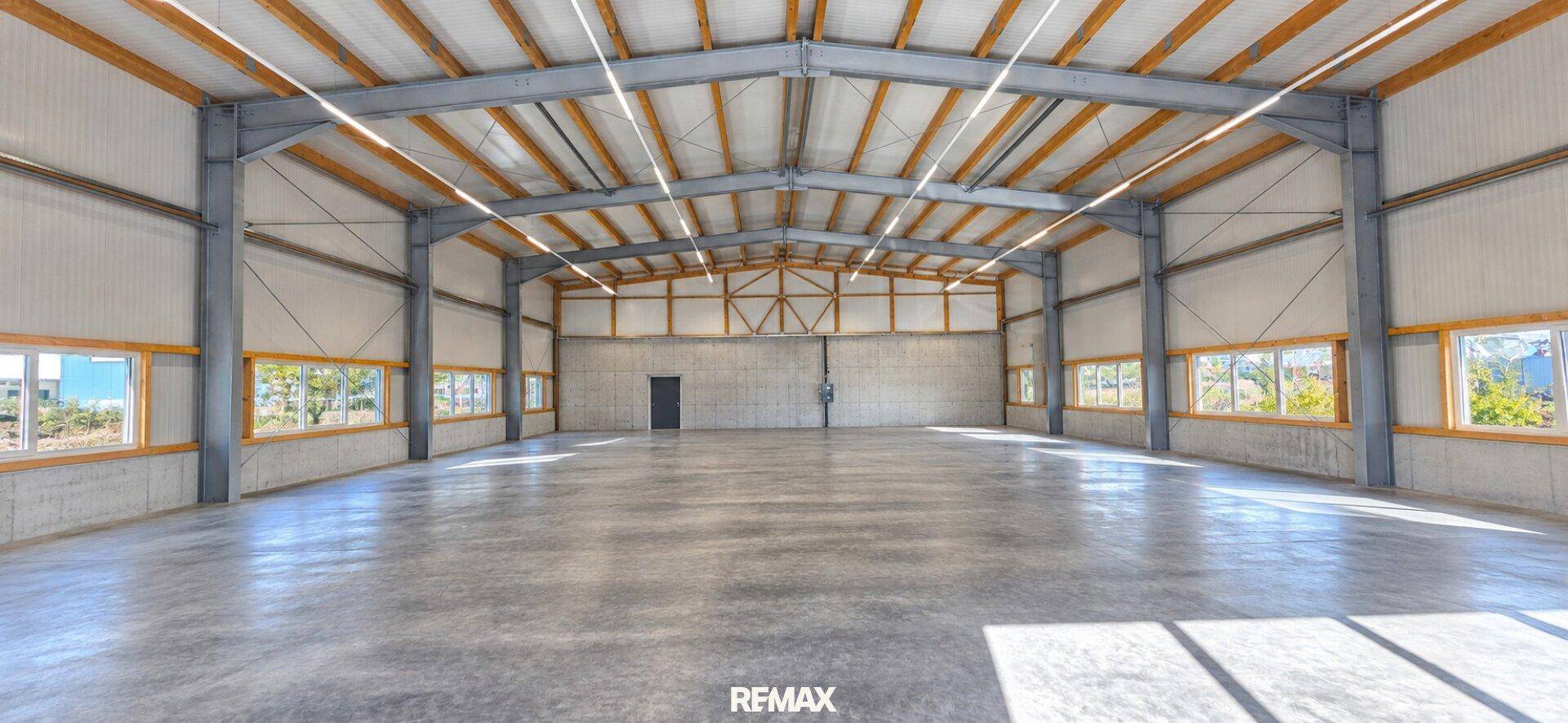 Geräumige, leere Lagerhalle mit hohen Decken, Betonboden und vielen Fenstern für natürliches Licht.