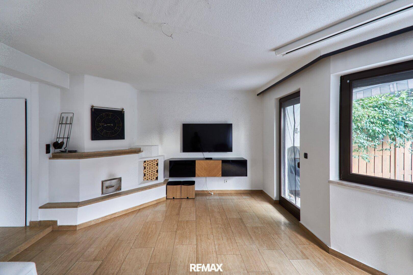 Helles Wohnzimmer mit modernem Kachelofen, Holzboden und Zugang zum Gartenbereich.