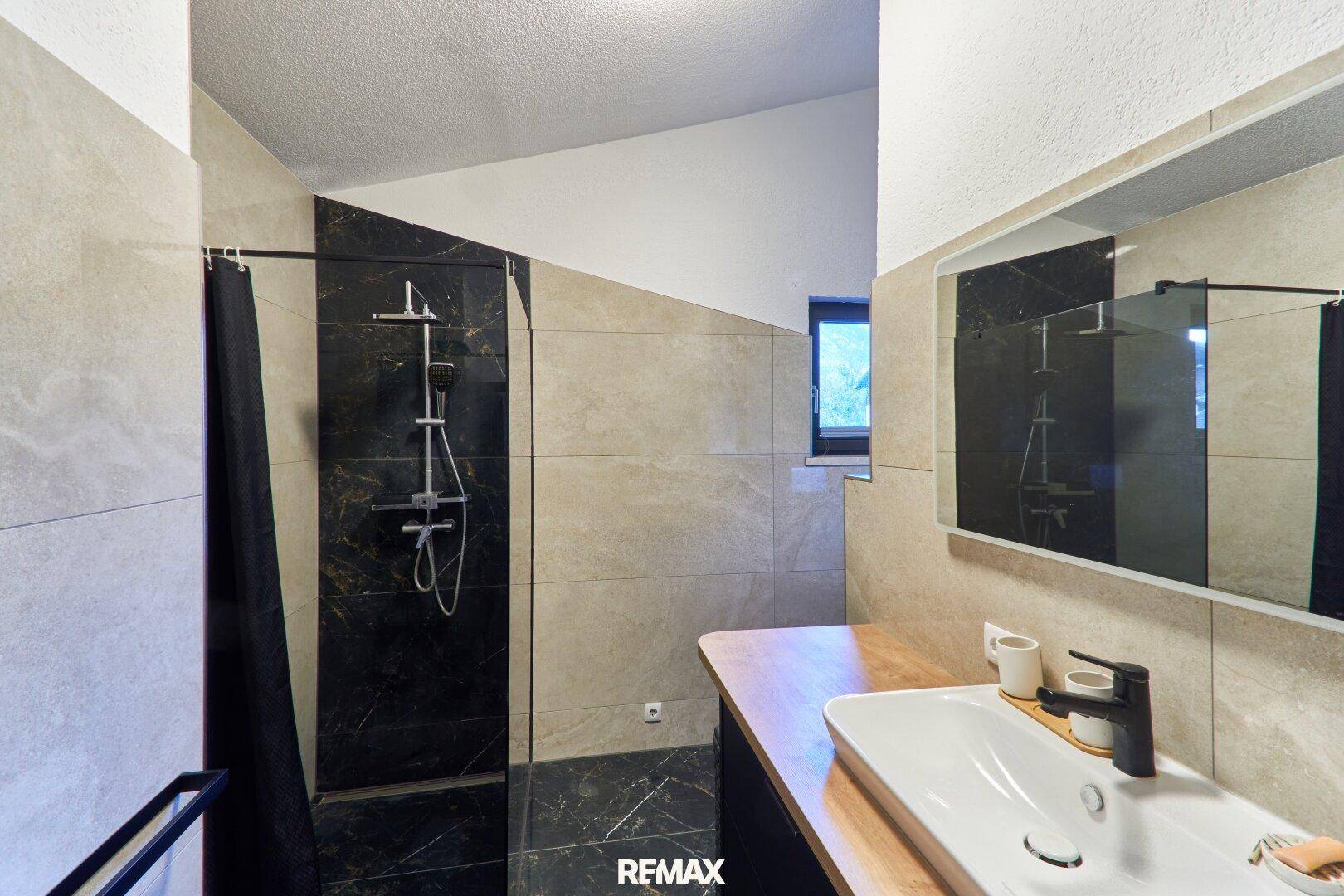 Modernes Badezimmer mit großformatigen Fliesen, begehbarer Dusche und Fenster für Tageslicht.