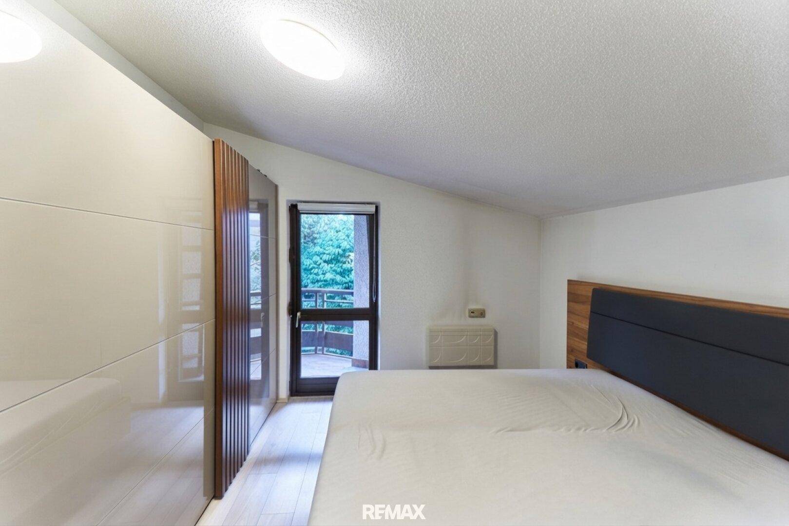 Schlafzimmer mit modernem Kleiderschrank, Holzboden und Zugang zu einem Außenbereich.
