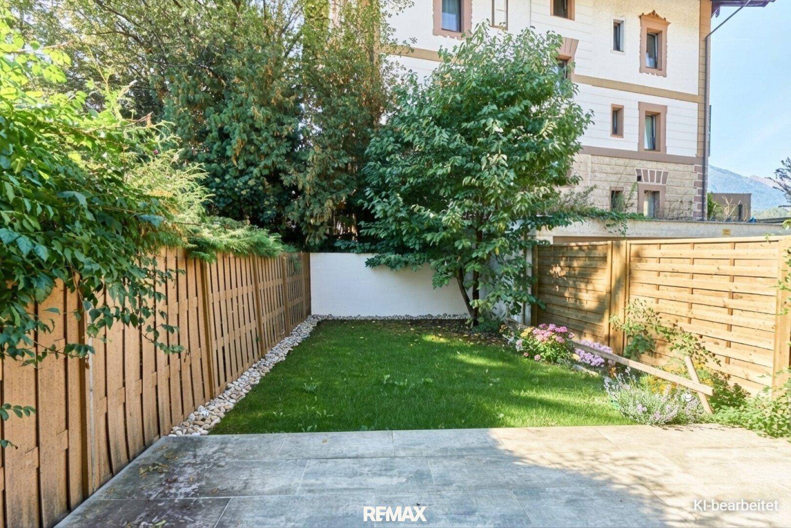 Kleiner, eingezäunter Gartenbereich mit Rasenfläche und gepflastertem Sitzbereich.