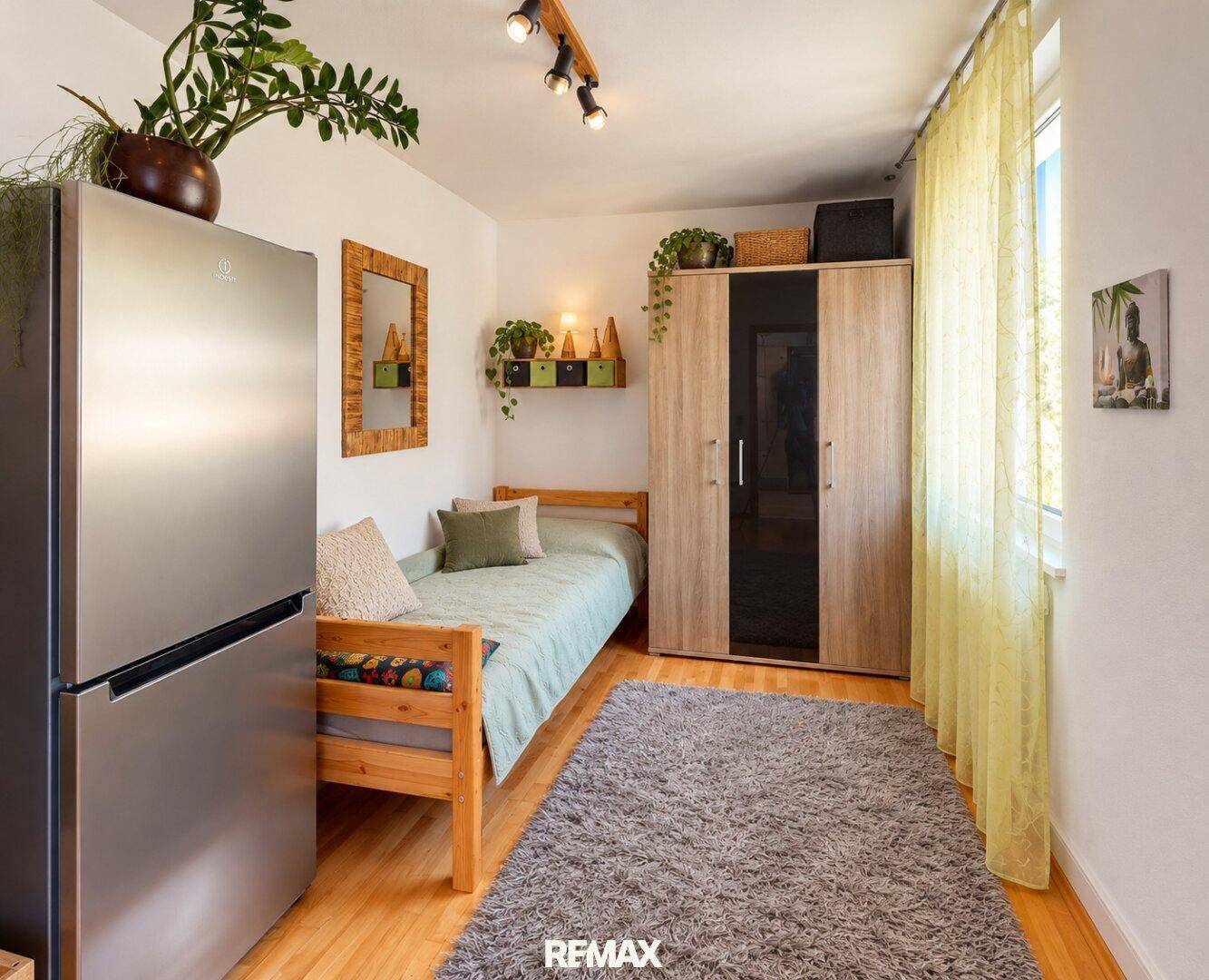 Helles Schlafzimmer mit Einzelbett, Kleiderschrank und einem Kühlschrank, funktional eingerichtet.