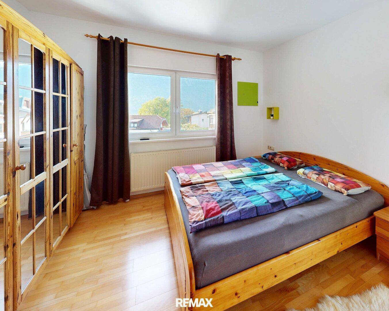 Geräumiges Schlafzimmer mit Doppelbett, Holzschrank und Fenster mit Blick ins Grüne.