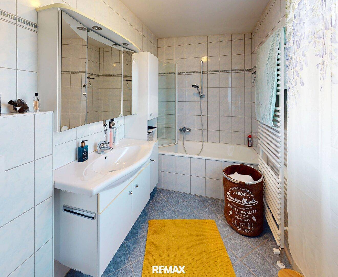 Helles Badezimmer mit Badewanne, Dusche, Waschbecken und Spiegelschrank, komplett gefliest.
