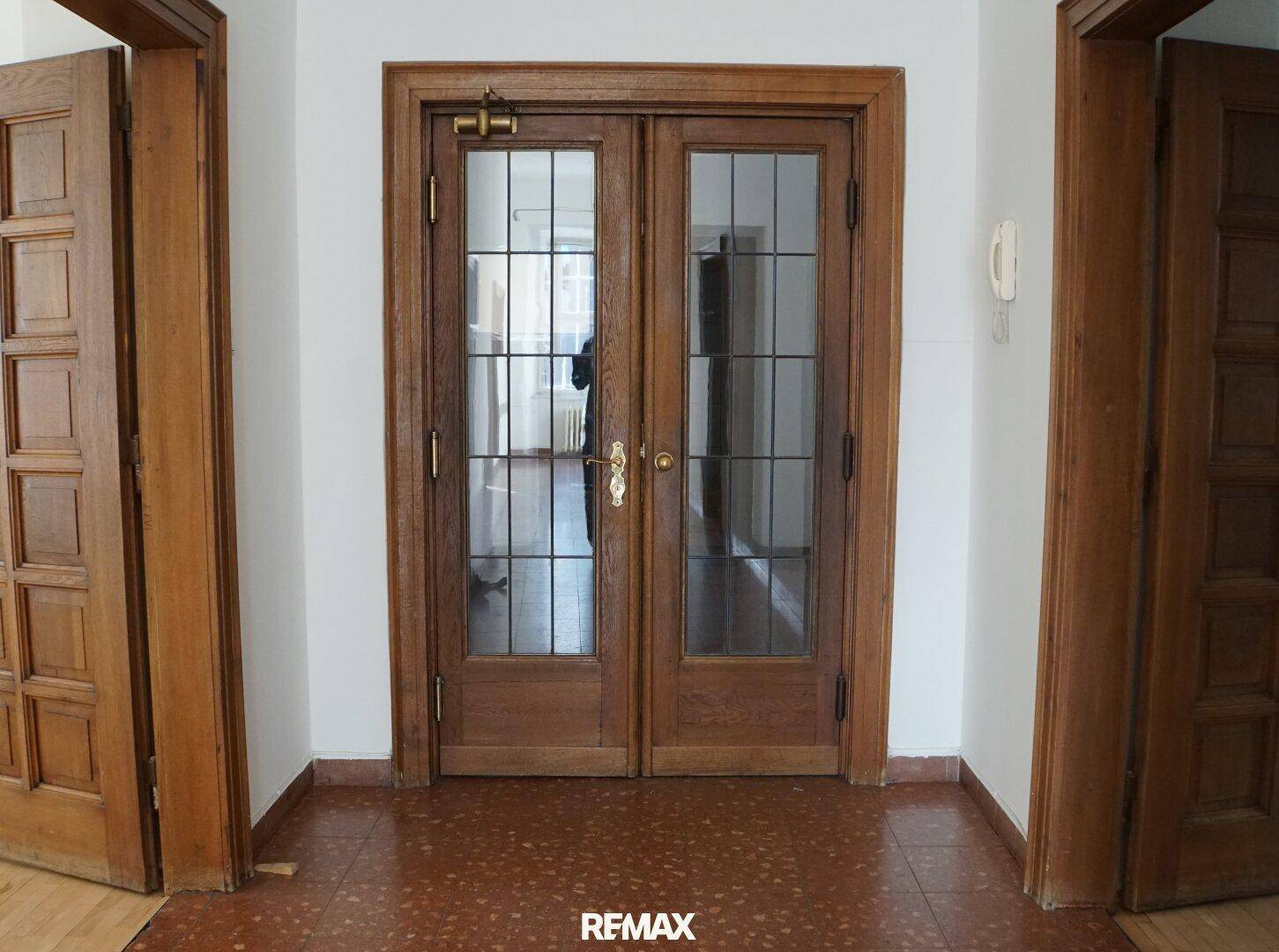 Eingangsbereich mit Terrakotta-Fliesenboden und eleganten Doppeltüren aus Holz mit Glaseinsätzen.