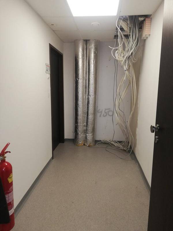 Flur mit sichtbaren Rohren, herabhängenden Elektrokabeln von der Decke und einem Feuerlöscher.
