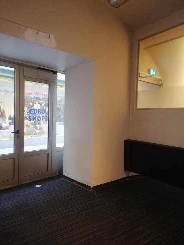 Ecke eines Raumes mit dunklem Teppichboden, Blick auf Glastüren und einem Spiegel, der eine gewölbte Decke reflektiert.