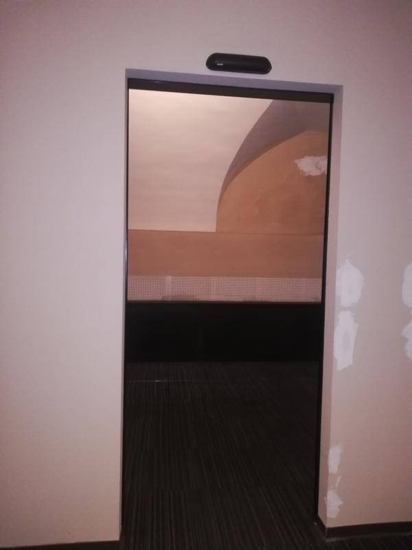 Blick durch einen Türrahmen in einen Bereich mit dunklem Boden und einer Reflexion einer gewölbten Decke.
