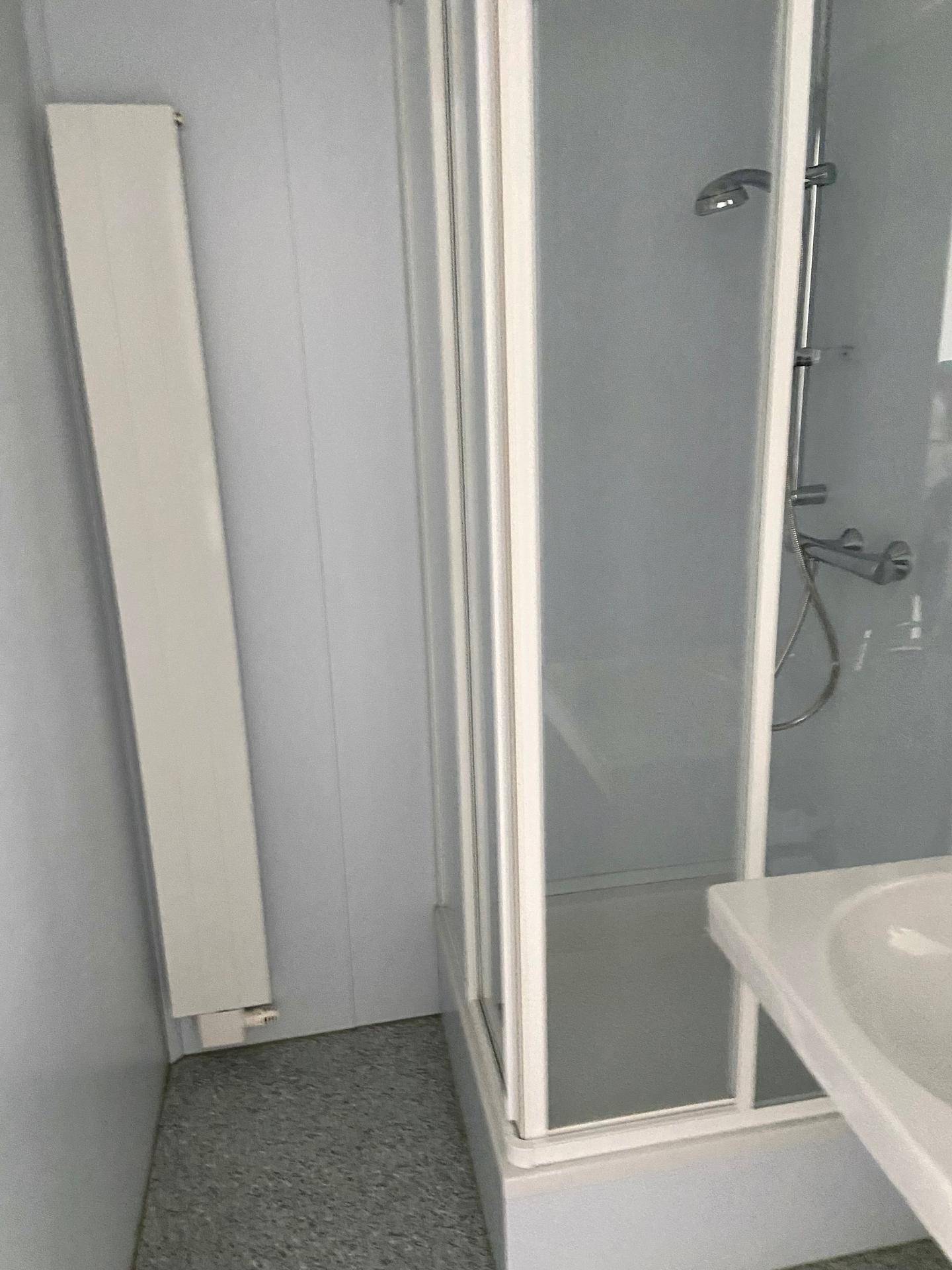 Duschkabine mit Glaswänden und einem Heizkörper in einem funktionalen Badezimmer.