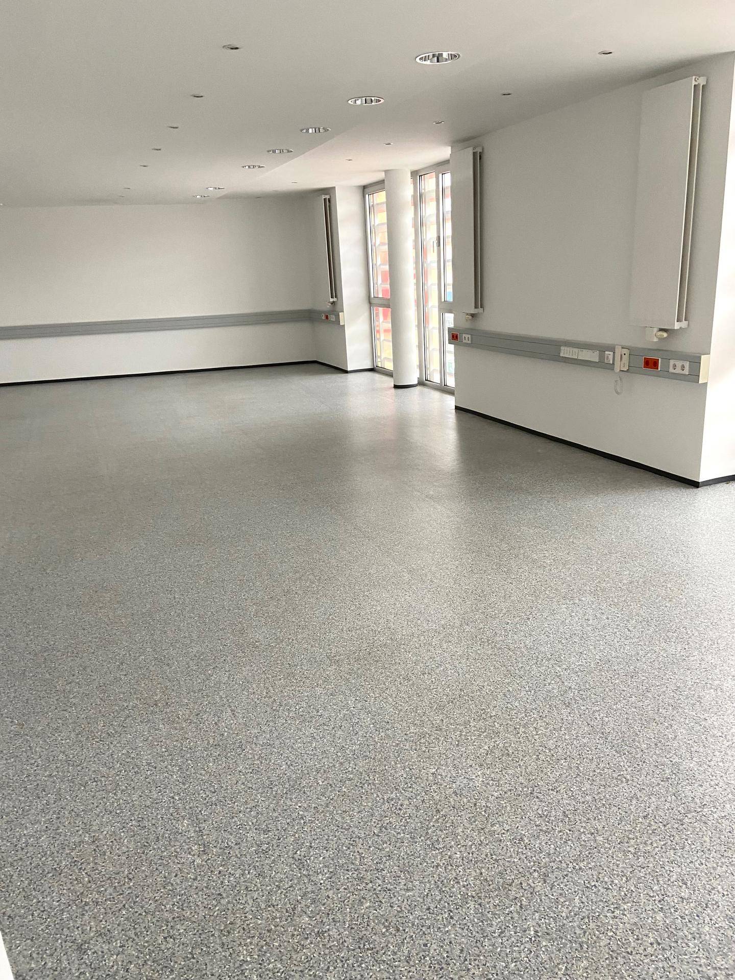 Heller, leerer Büroraum mit großen Fenstern, modernem Bodenbelag und Wandanschlüssen.