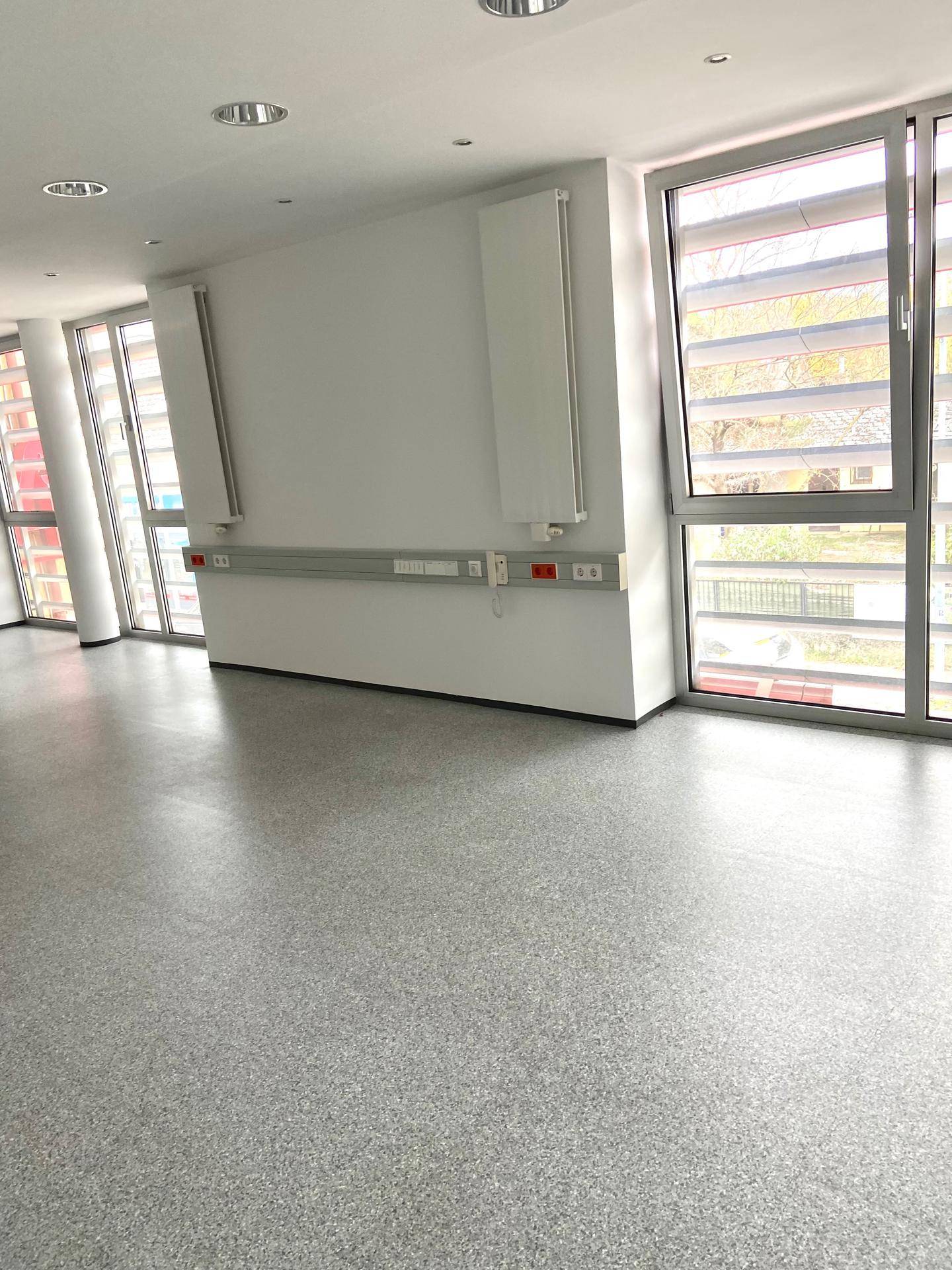 Geräumiger, heller Büroraum mit großen Fenstern, modernem Bodenbelag und Wandanschlüssen.