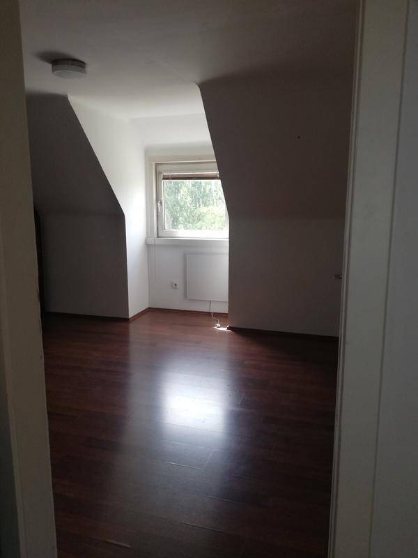 Schlafzimmer mit dunklem Laminatboden, Dachschrägen und einem Fenster, das natürliches Licht hereinlässt.