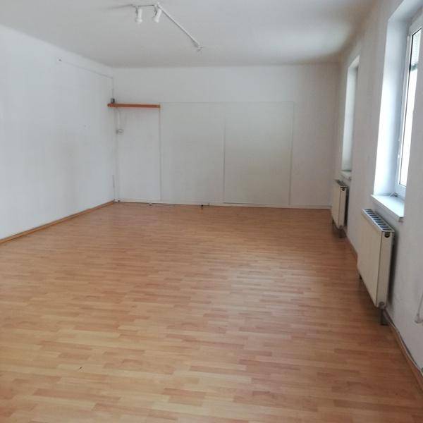 Leerer Raum mit Laminatboden, weißen Wänden und Heizkörpern unter den Fenstern.