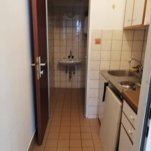 Kleine Küchenzeile mit Spüle und Kochfeld, daneben ein gefliester Bereich mit Waschbecken.