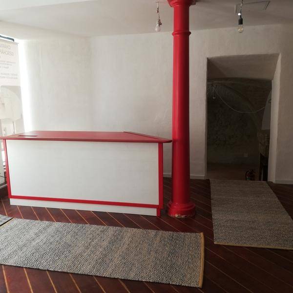 Verkaufsraum mit roter Säule, Empfangstheke und einem Durchgang zu einem Bereich mit Gewölbedecke.