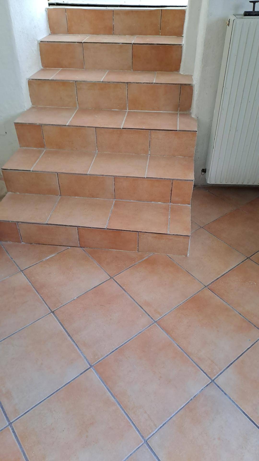 Geflieste Treppe und Boden in einem Innenbereich mit Heizkörper an der Wand.